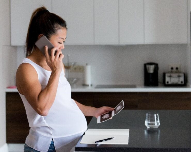 Pregnant woman talks on phone while looking at sonogram image - stock photo