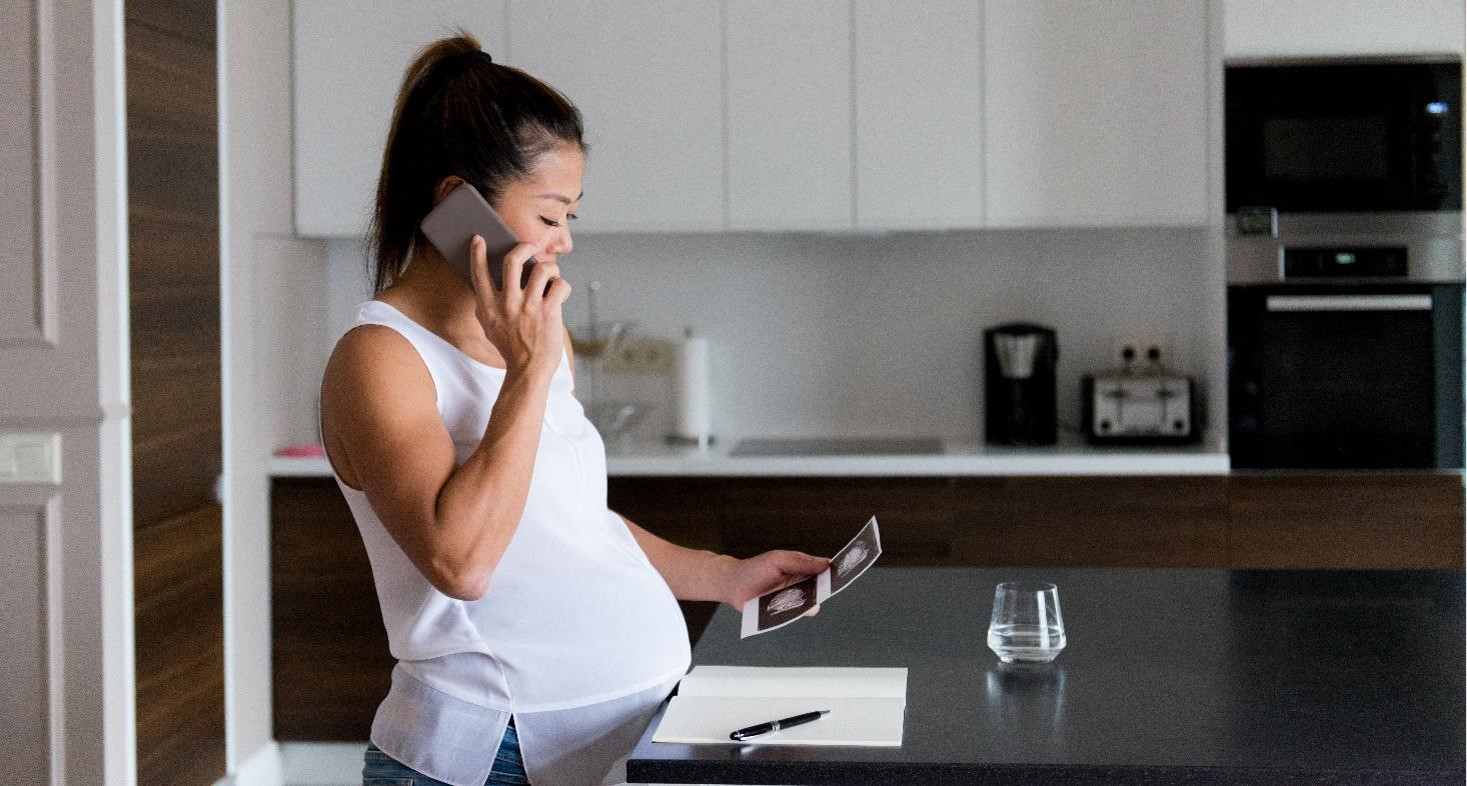 Pregnant woman talks on phone while looking at sonogram image - stock photo