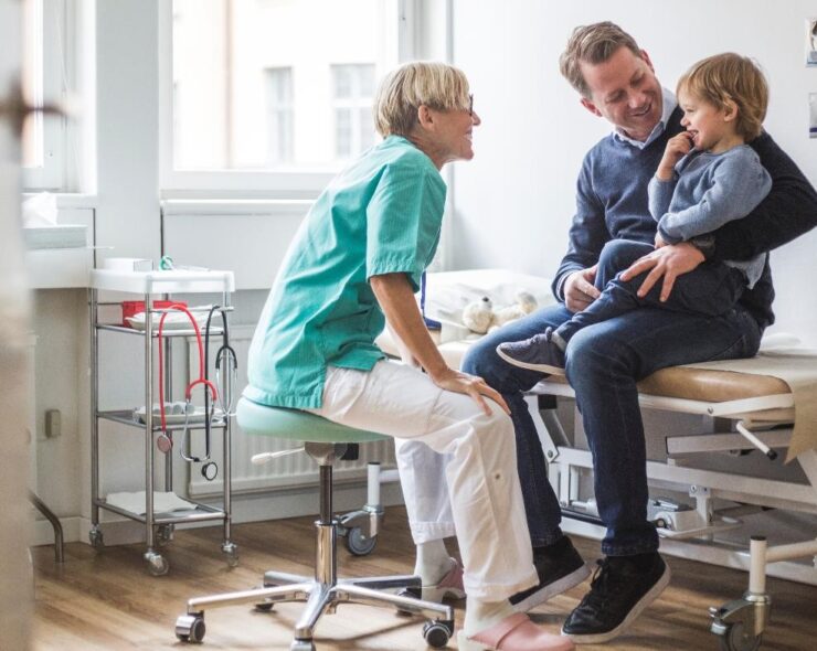 Side view of smiling female doctor talking to boy with father in clinic