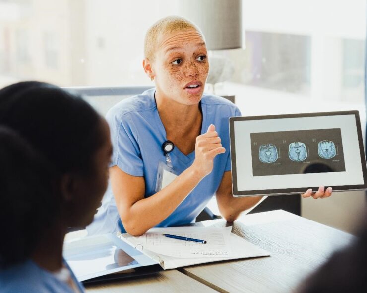 A confident female neurologist discusses a patient's brain scan with a group of colleagues.