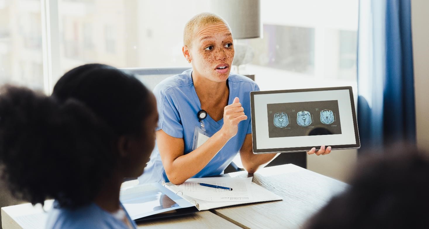 A confident female neurologist discusses a patient's brain scan with a group of colleagues.