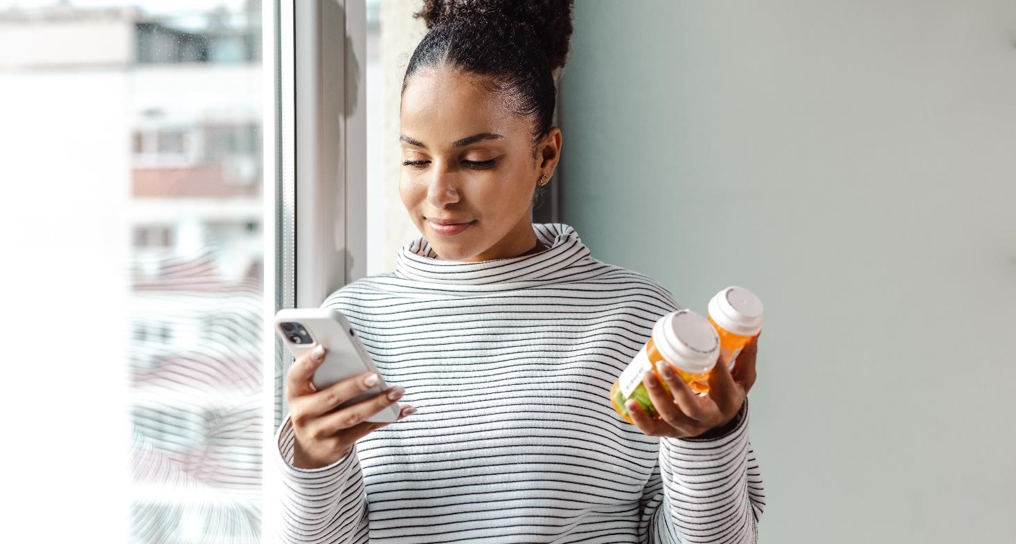 A young happy woman holding a smart phone and a pill bottle
