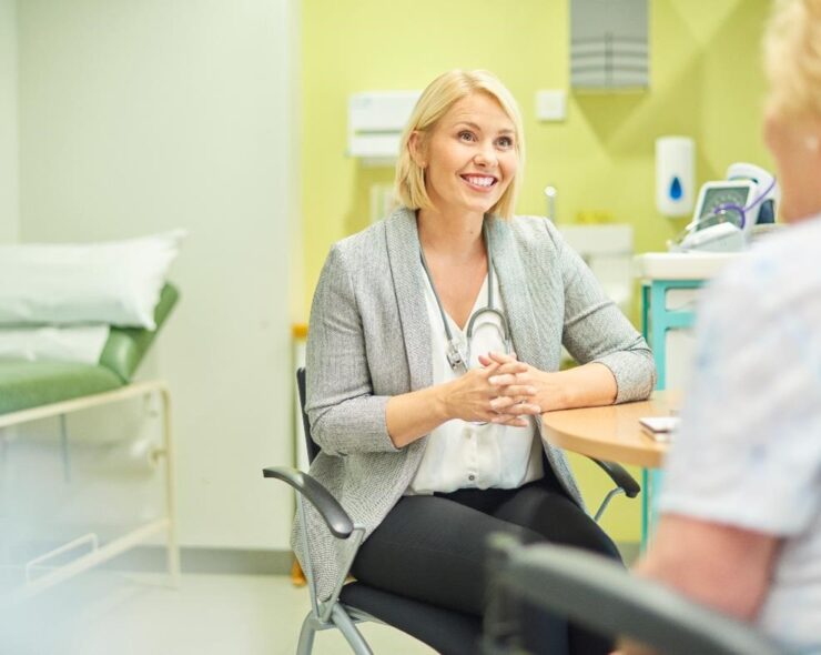 A blonde female doctor sitting with a patient at a table, smiling
